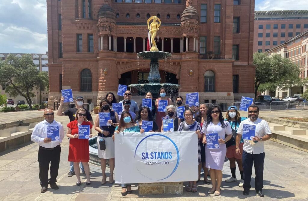 A photo of a group of people holding a sign saying "SA STANDS" in Bexar County, Texas after the creation of an immigrant legal defense fund.