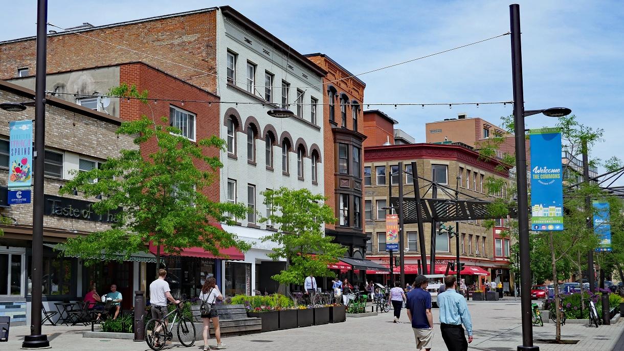 A photograph of downtown Ithaca, New York featuring old buildings and pedestrians walking and biking along the street.