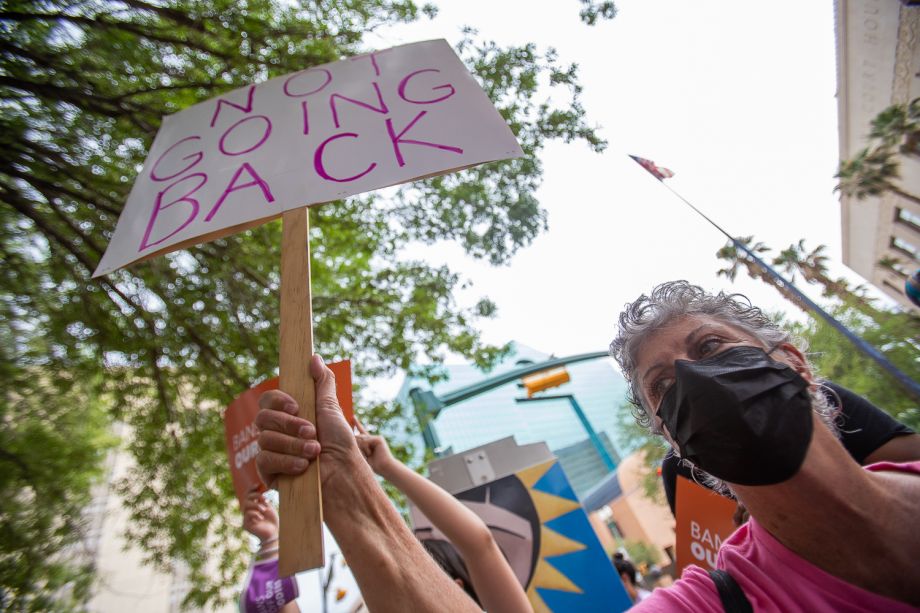 A masked person holding up a sign that says "not going back."